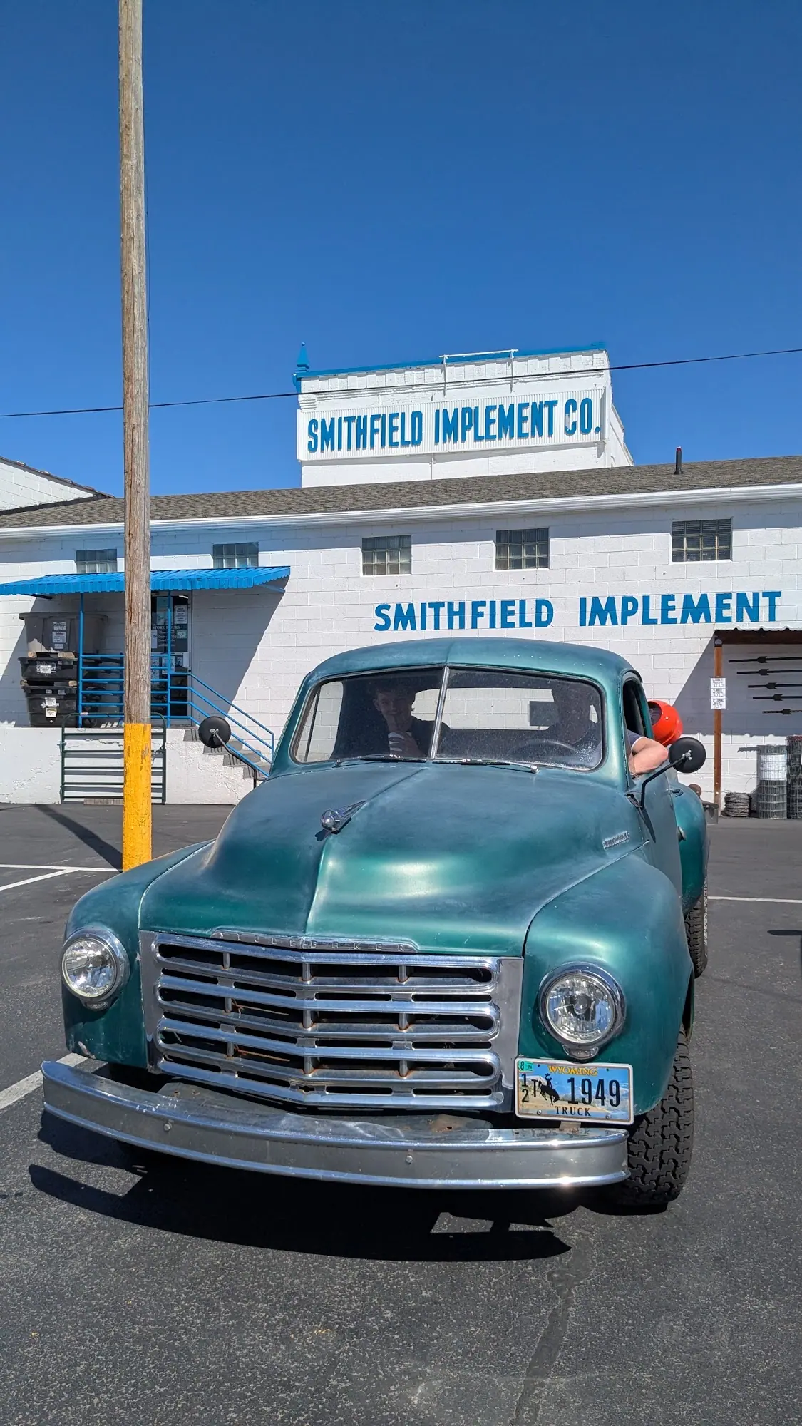 A turquoise vintage pickup parked in front of the Smithfield Implement sign
